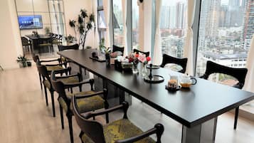 A modern conference room with a long table, chairs, and a city view through large windows.