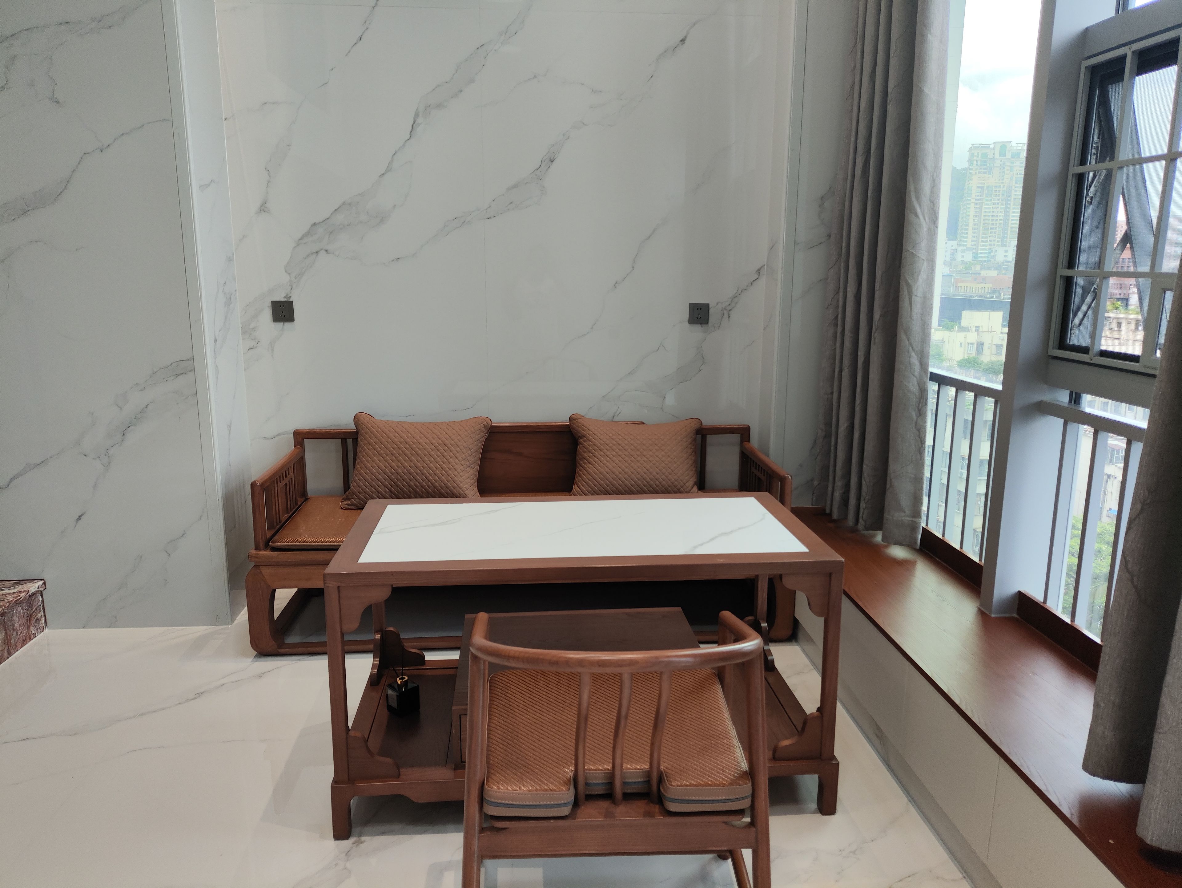Une pièce moderne avec un mur en marbre, un canapé en bois avec des coussins, une table à manger et une chaise.