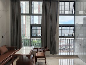 A room with a large window, a wooden table, a sofa, and a chair. - Healing Warm Home (Shen Zhen Shi)