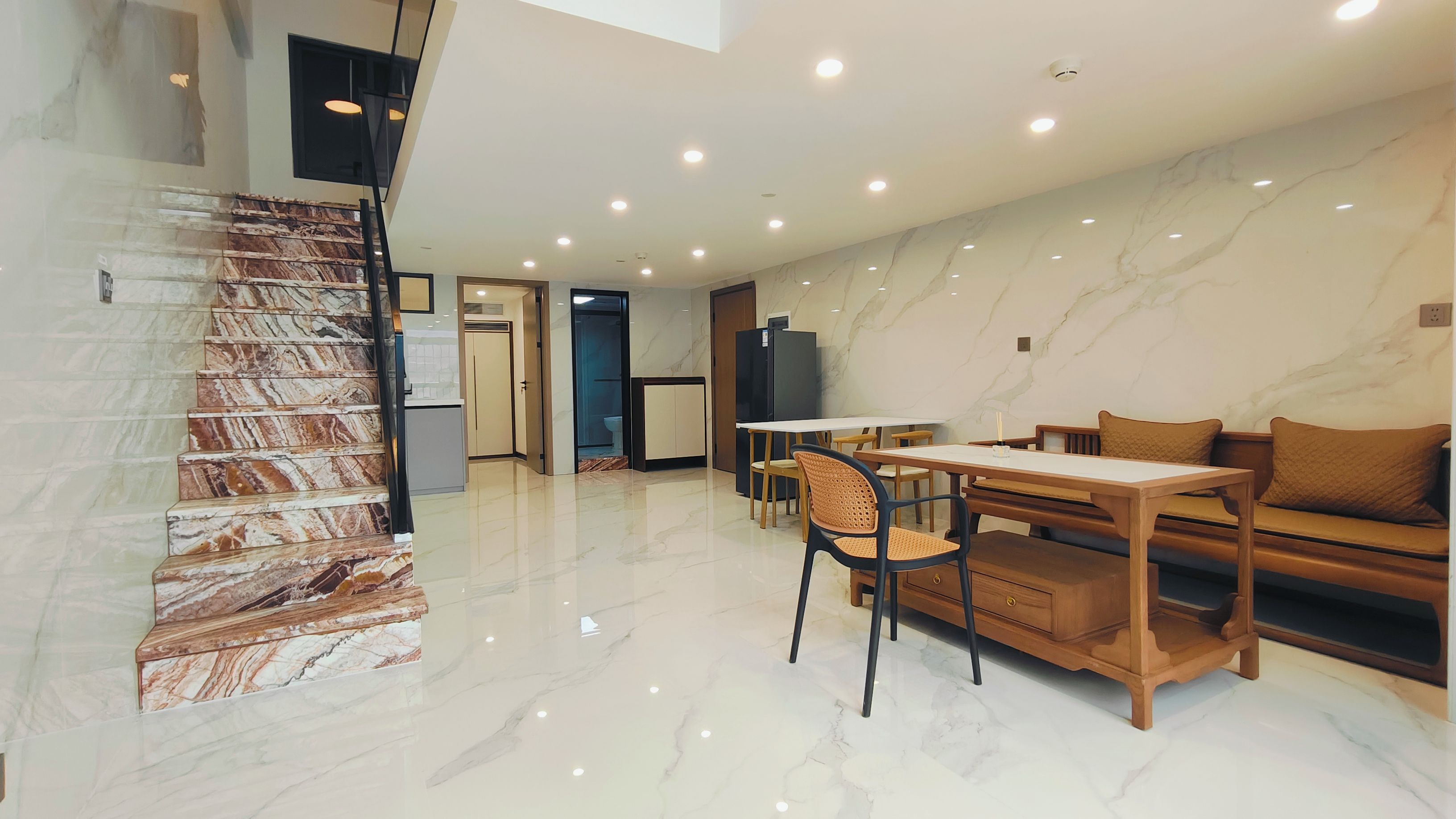 A modern interior with a marble staircase, a dining area with wooden furniture, and a kitchen area.