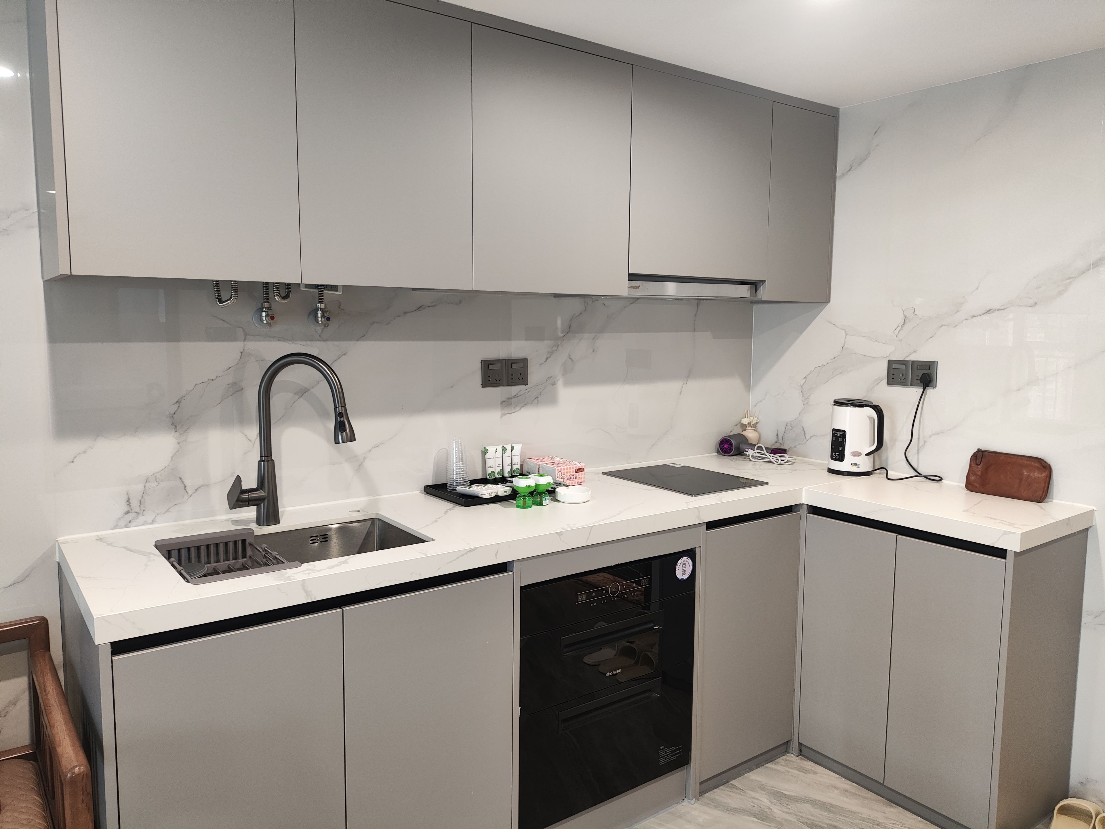 A modern kitchen with grey cabinets, a stainless steel sink, a built-in oven, and a coffee maker.
