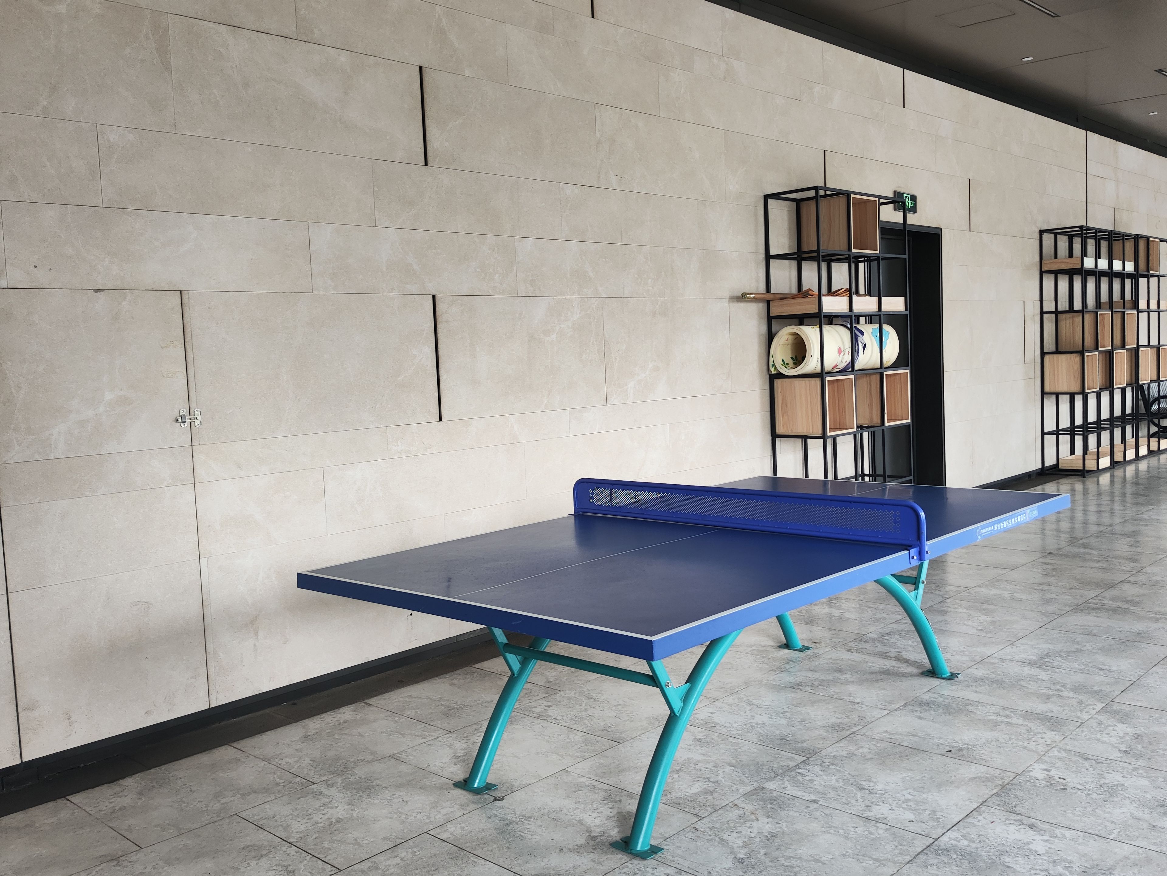 A ping pong table in a hallway with tiled flooring and a wall with a geometric pattern.