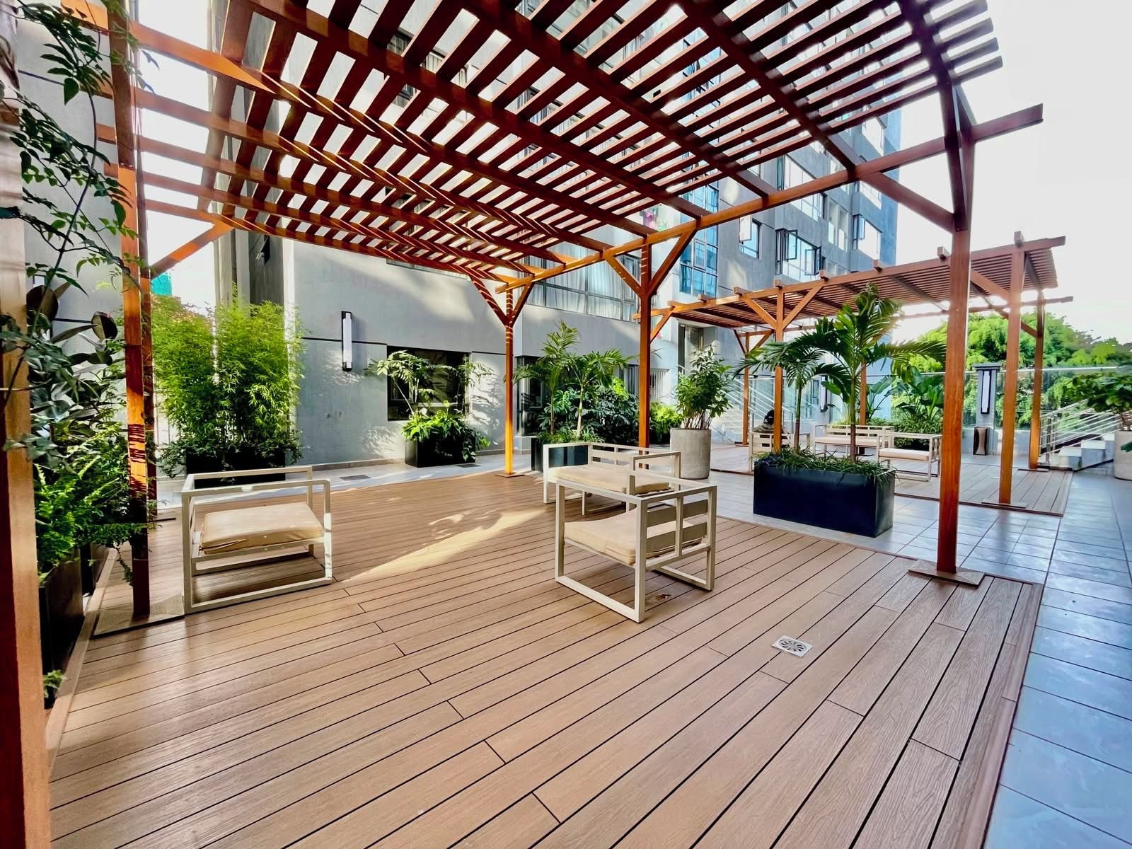 An outdoor patio area with wooden flooring, seating arrangements, and potted plants.