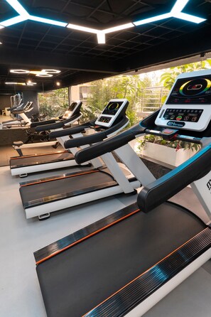Eine Reihe von Laufbändern in einem Fitnessstudio mit einem digitalen Display, einer Decke mit geometrischer Beleuchtung und Blick auf Grünflächen im Freien.