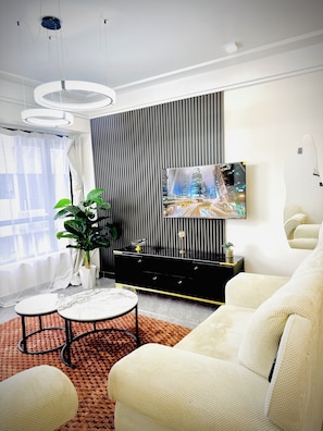 A modern living room with a flat-screen TV, a black entertainment unit, a large potted plant, and a beige sofa. - Elagant 2BR in lavington/kilimani/kileleshwa w/pool gym near malls central place (Nairobi)