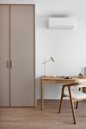 A minimalist room with a wooden desk, a white chair, a standing lamp, and an air conditioning unit. - Chronos Prestige Suite & Parking by Downtown Apartments (Warszawa)