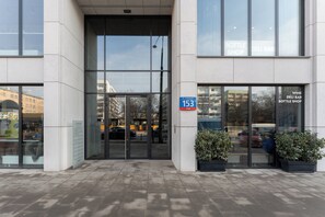 A building entrance with a glass door, a sign indicating the address '153', and a window advertising a wine deli bar and bottle shop. - Chronos Prestige Suite & Parking by Downtown Apartments (Warszawa)
