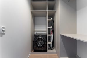 A laundry room with a washing machine, shelves, and a power outlet. - Chronos Prestige Suite & Parking by Downtown Apartments (Warszawa)