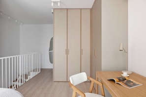 A modern, minimalist room with a wooden floor, a white crib, a wooden dining table with a magazine, and a wardrobe with sliding doors. - Chronos Prestige Suite & Parking by Downtown Apartments (Warszawa)
