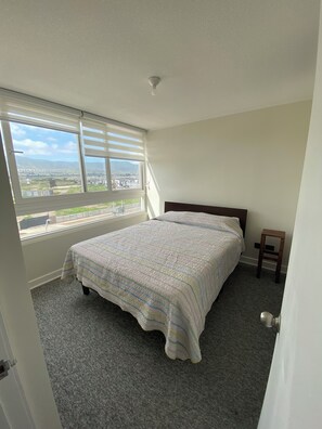 Ein Schlafzimmer mit einem großen Bett, einem kleinen Hocker und einem Fenster mit Blick auf die Stadt.