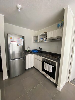 A compact kitchen with a stainless steel refrigerator, a stove, and a sink. - Vive La Serena con comodidad y estilo. Departamento nuevo completamente equipado (La Serena)