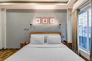 Habitación de hotel con cama, dos mesitas de noche, una lámpara de noche, ventana con cortinas y tres cuadros en la pared.