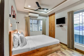 Un dormitorio con cama, ventilador de techo, televisión y ventana con cortinas.