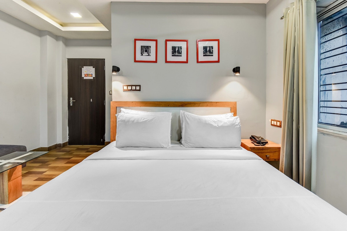 Een hotelkamer met een bed, een nachtkastje met een telefoon, een wandlamp en drie ingelijste foto's boven het bed.