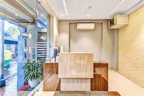 Een receptiebalie met een houten afwerking, een wandairconditioner en een glazen deur met weerspiegeling van de straat.