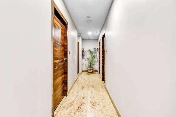 Un pasillo con puertas de madera, una planta en maceta y suelo de mármol.