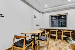 Una habitación con una mesa redonda y cuatro sillas de madera con cojines negros, una ventana con barrotes de metal y un enchufe de pared.