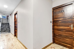 Un pasillo con dos puertas de madera, una escalera con baldosas blancas y negras y una pared blanca con un televisor montado.
