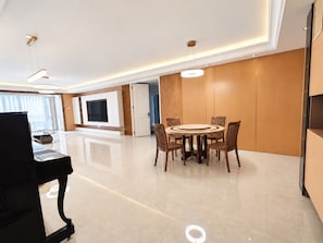 Una sala de estar moderna con un televisor de pantalla plana, una mesa de comedor con sillas y un piano.