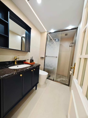 Un baño moderno con tocador negro, lavabo blanco y cabina de ducha con mampara de vidrio.