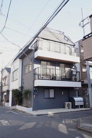 A modern two-story building with a balcony, air conditioning units, and a small garden area. - ISSHUKU Toshima ikebukuro3 (Toshima-ku)