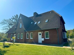 Ein zweistöckiges Haus mit geneigtem Dach, zahlreichen Fenstern und einer Haustür.