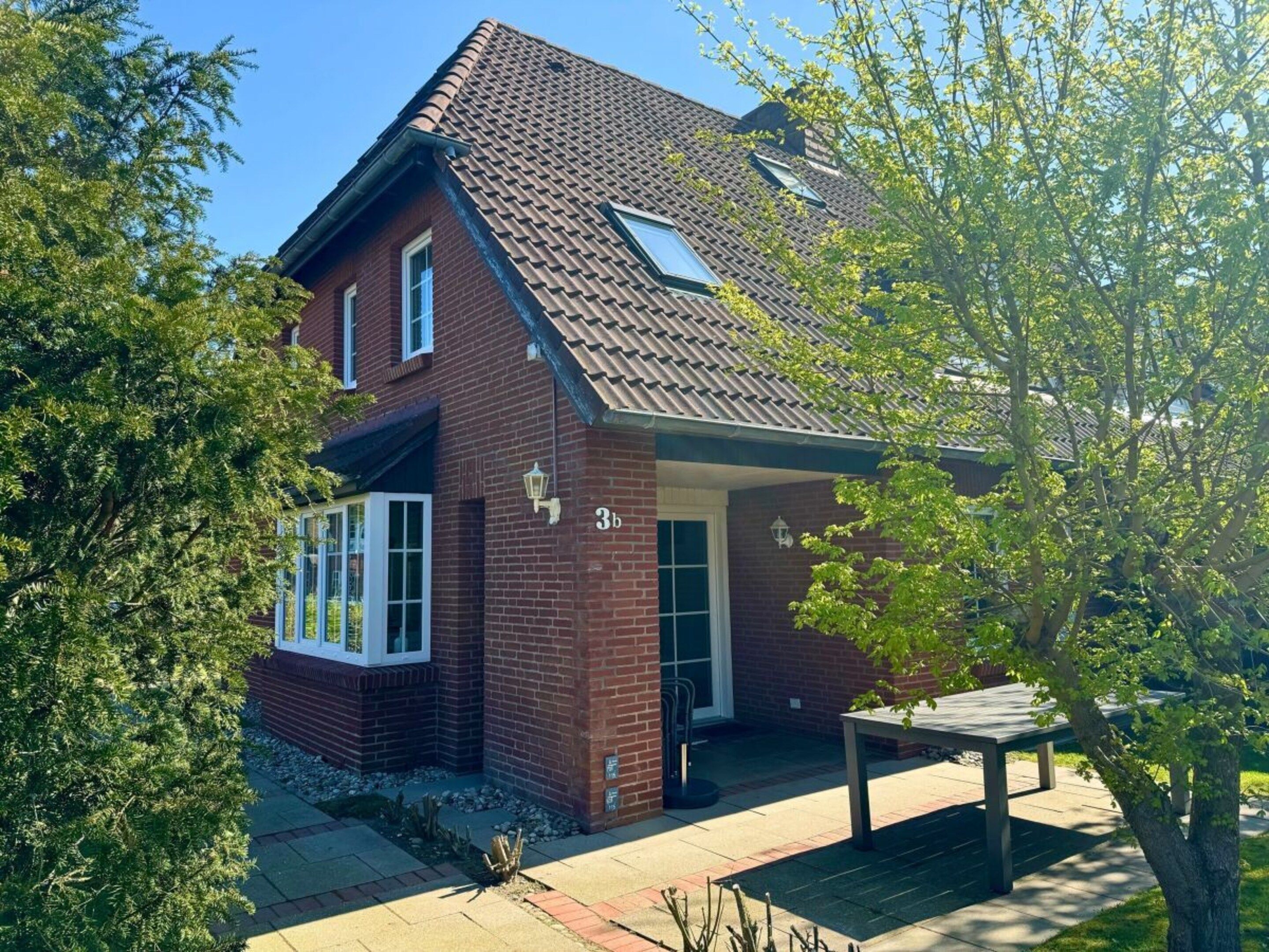 Ein zweistöckiges Backsteinhhaus mit geneigtem Dach, einer Veranda und einer kleinen Terrasse.