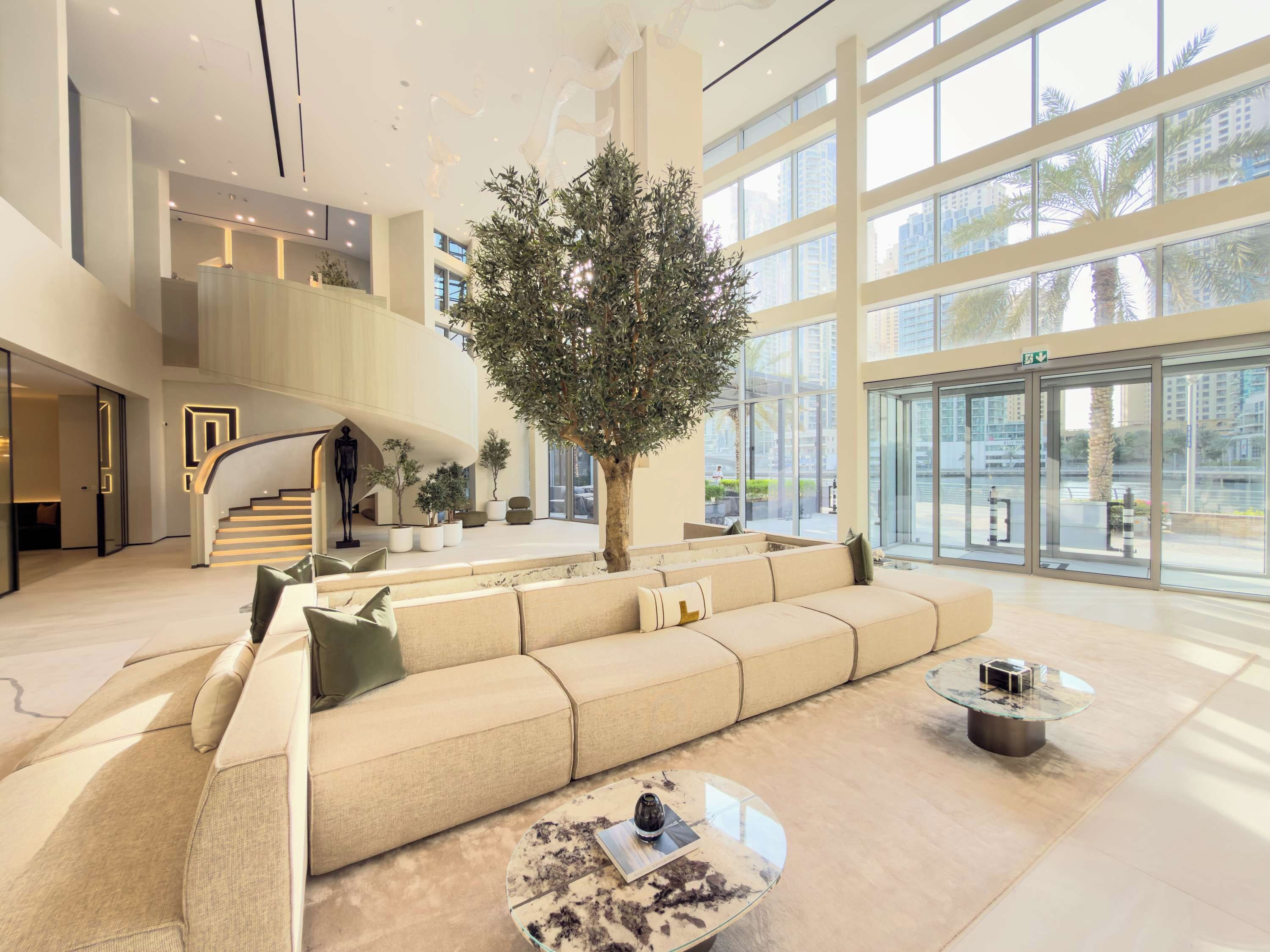 A spacious lobby with a large seating area, a staircase, and a view of the city through large windows.