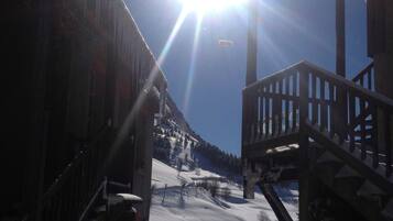 Ett snötäckt landskap med en trätrappa som leder upp till en balkong, en klar himmel och ett avlägset berg.