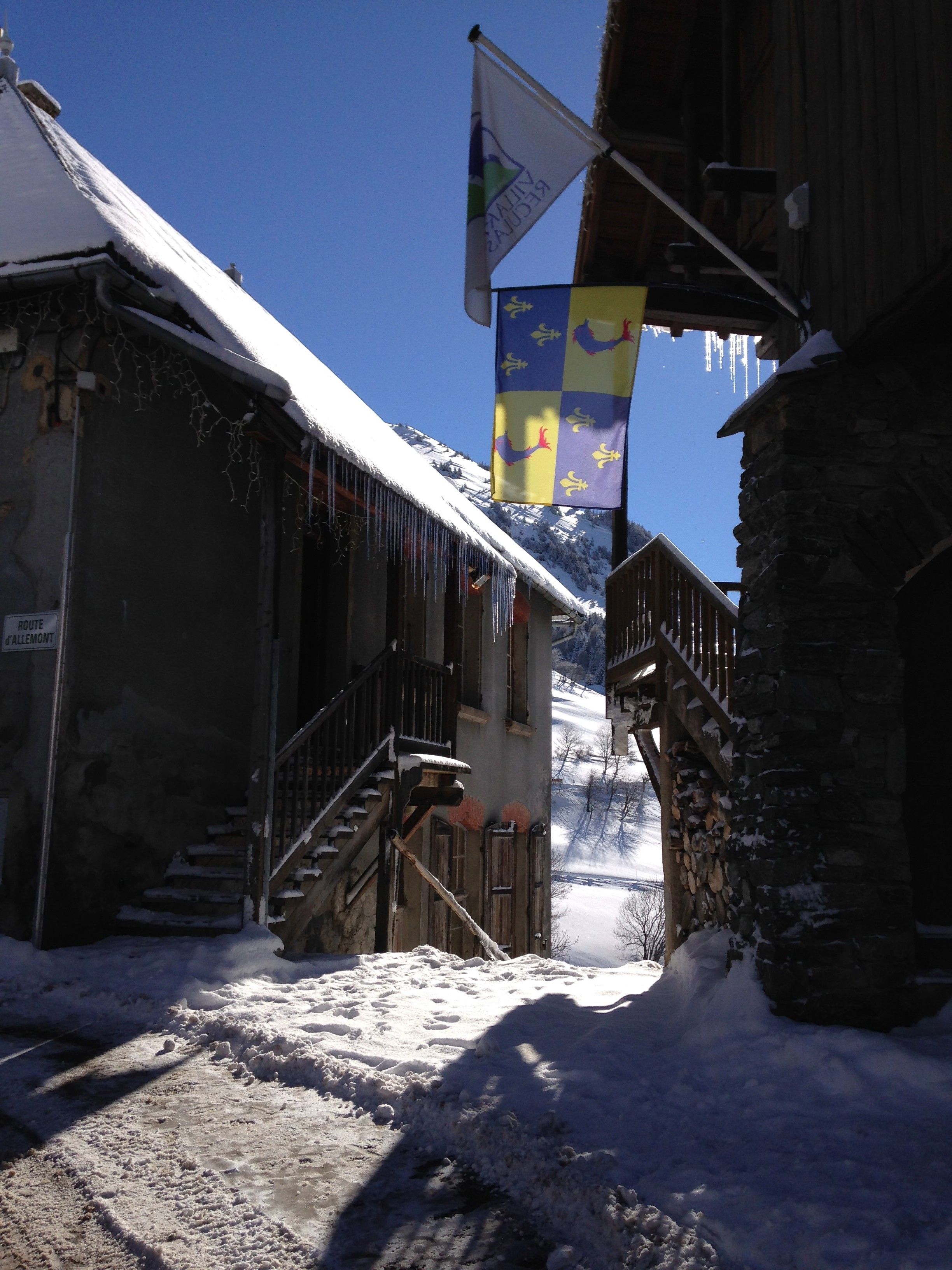 A snow-covered street with buildings, a flag, and a mountain in the background.