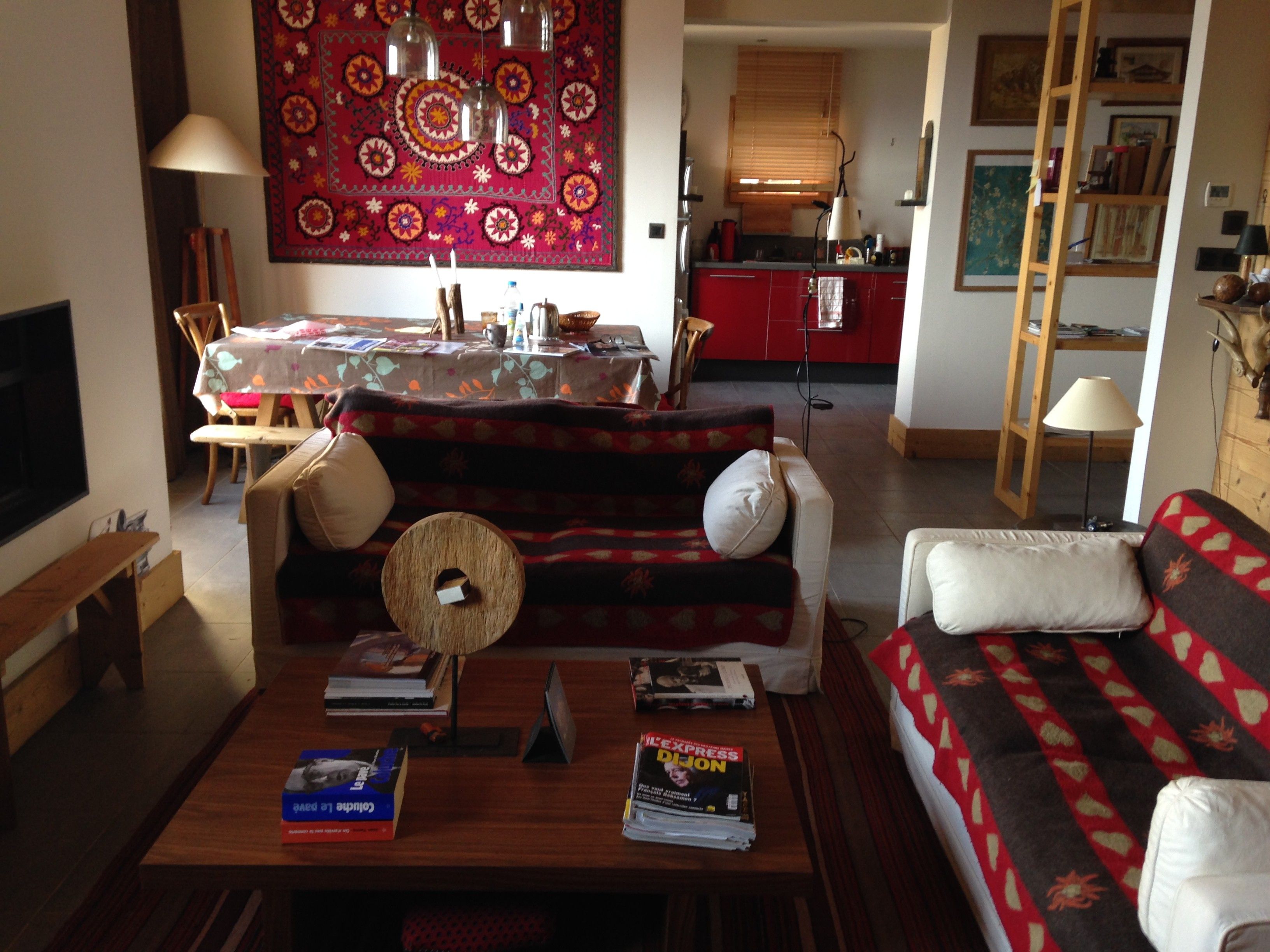 Ein Wohnzimmer mit einer Couch, einem Couchtisch mit Büchern, einem Fernseher und einer Wand mit rotem Muster.