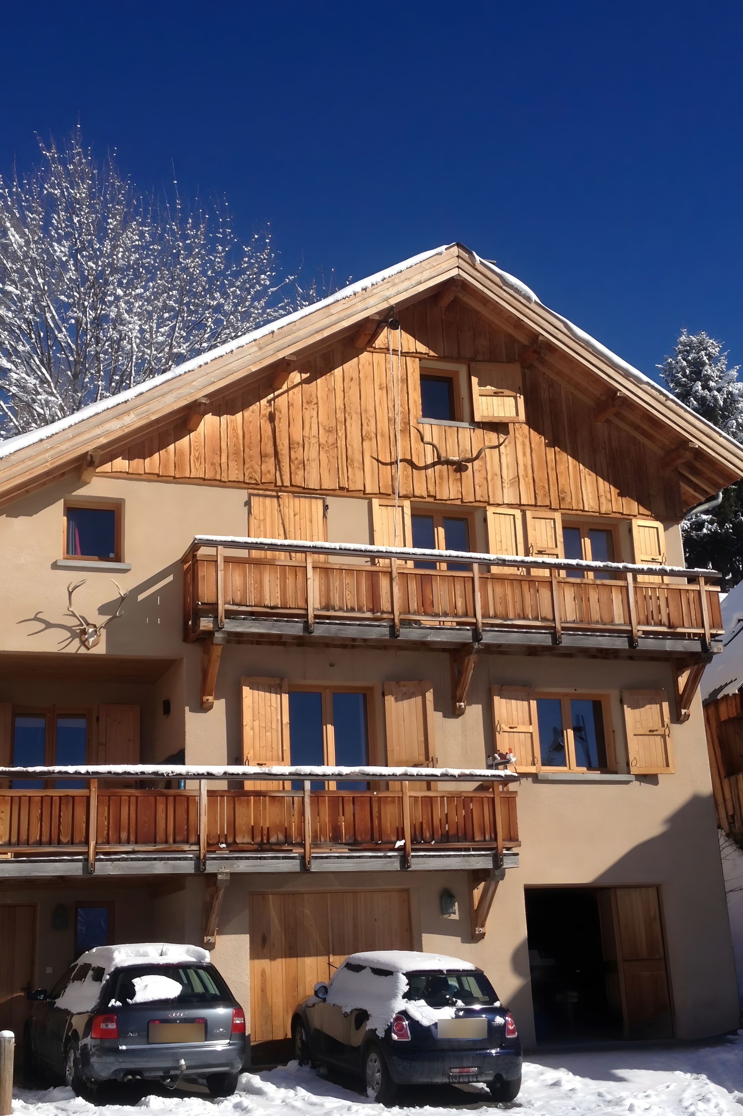 Ein mehrstöckiges Holzgebäude mit Balkonen, ein Auto davor und Schnee auf dem Dach und Boden.