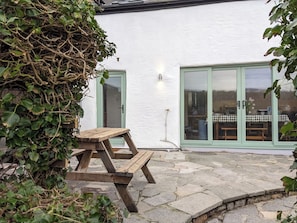 A wooden picnic table in front of a white building with green-framed glass doors. - Coastal Cottage - Beach - Parking - Pet friendly (Broad Haven)