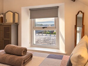 A bedroom with a large window, a bed with a rolled-up towel, a dresser, and a mirror. - Coastal Cottage - Beach - Parking - Pet friendly (Broad Haven)