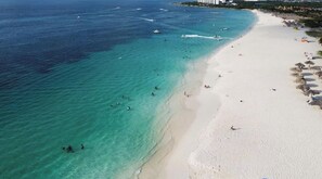 Une plage à l’eau turquoise et limpide, un rivage sablonneux et quelques parasols.