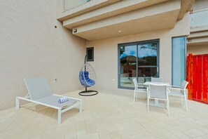 A patio with a white lounge chair, a hanging chair, and a table with chairs. - Walishali ONE17 • Chic 1BR Condo w/ Resort Access (Noord)