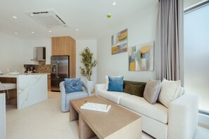 A modern living room with a sofa, coffee table, and a dining area with a kitchen in the background. - Walishali ONE17 • Chic 1BR Condo w/ Resort Access (Noord)