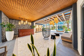 A modern lobby with a wooden ceiling, patterned wall, and seating area with a view of the pool. - Walishali ONE17 • Chic 1BR Condo w/ Resort Access (Noord)
