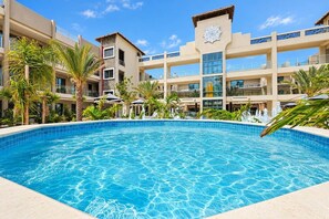 Um hotel com uma grande piscina, palmeiras e um edifício moderno com fachada decorativa.