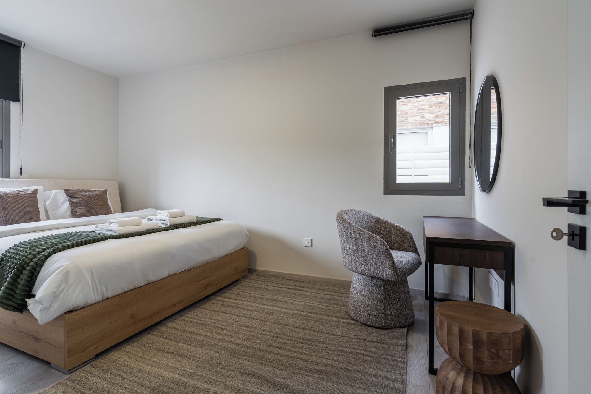 A bedroom with a bed, a chair, a desk, and a window.