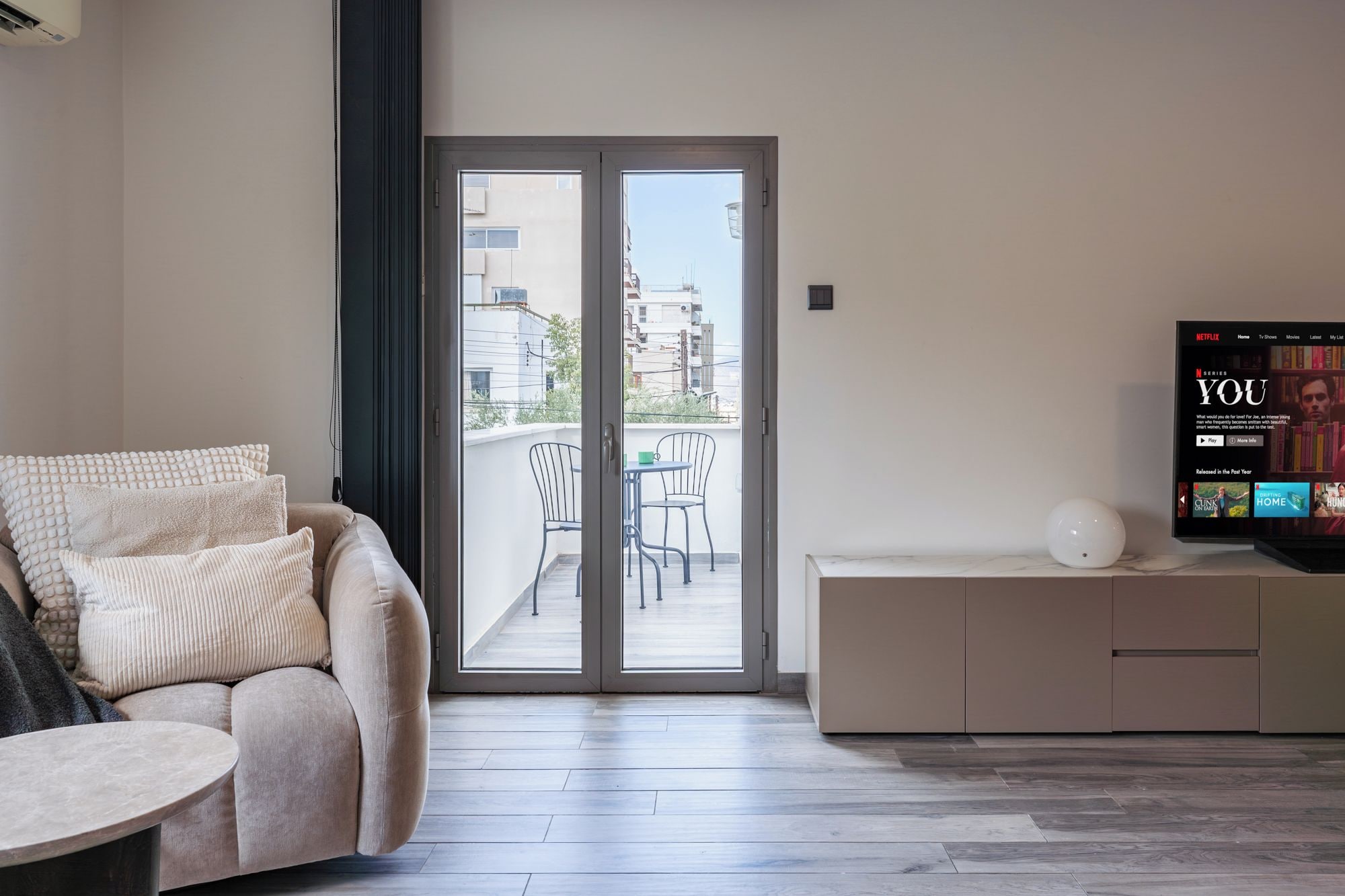 A modern living room with a sofa, a coffee table, a TV, and a sliding glass door leading to an outdoor balcony.