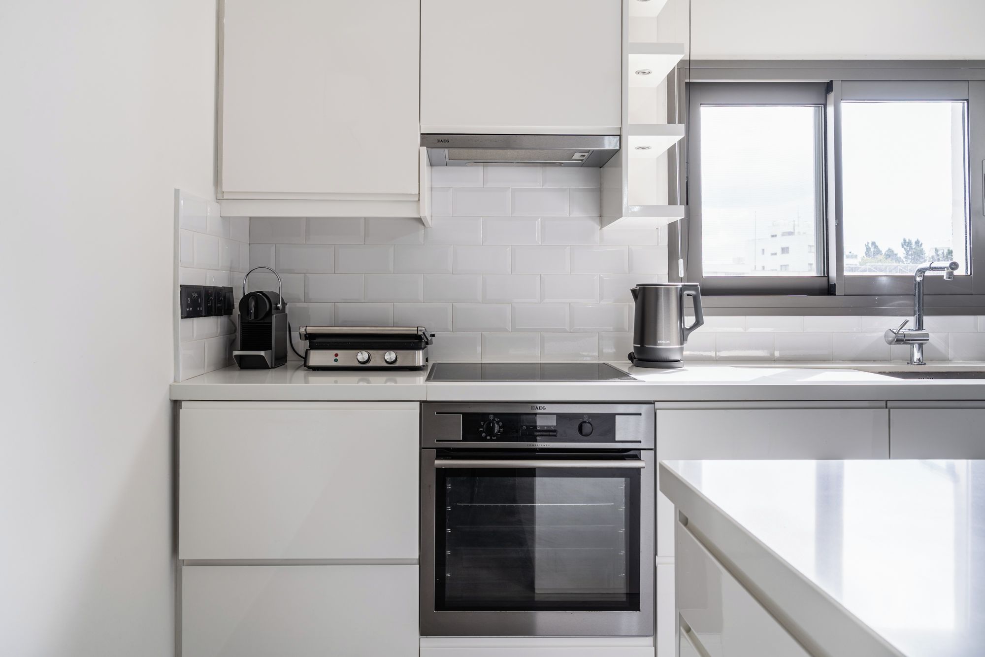 Una cocina moderna con armarios blancos, horno empotrado y ventana que proporciona luz natural.