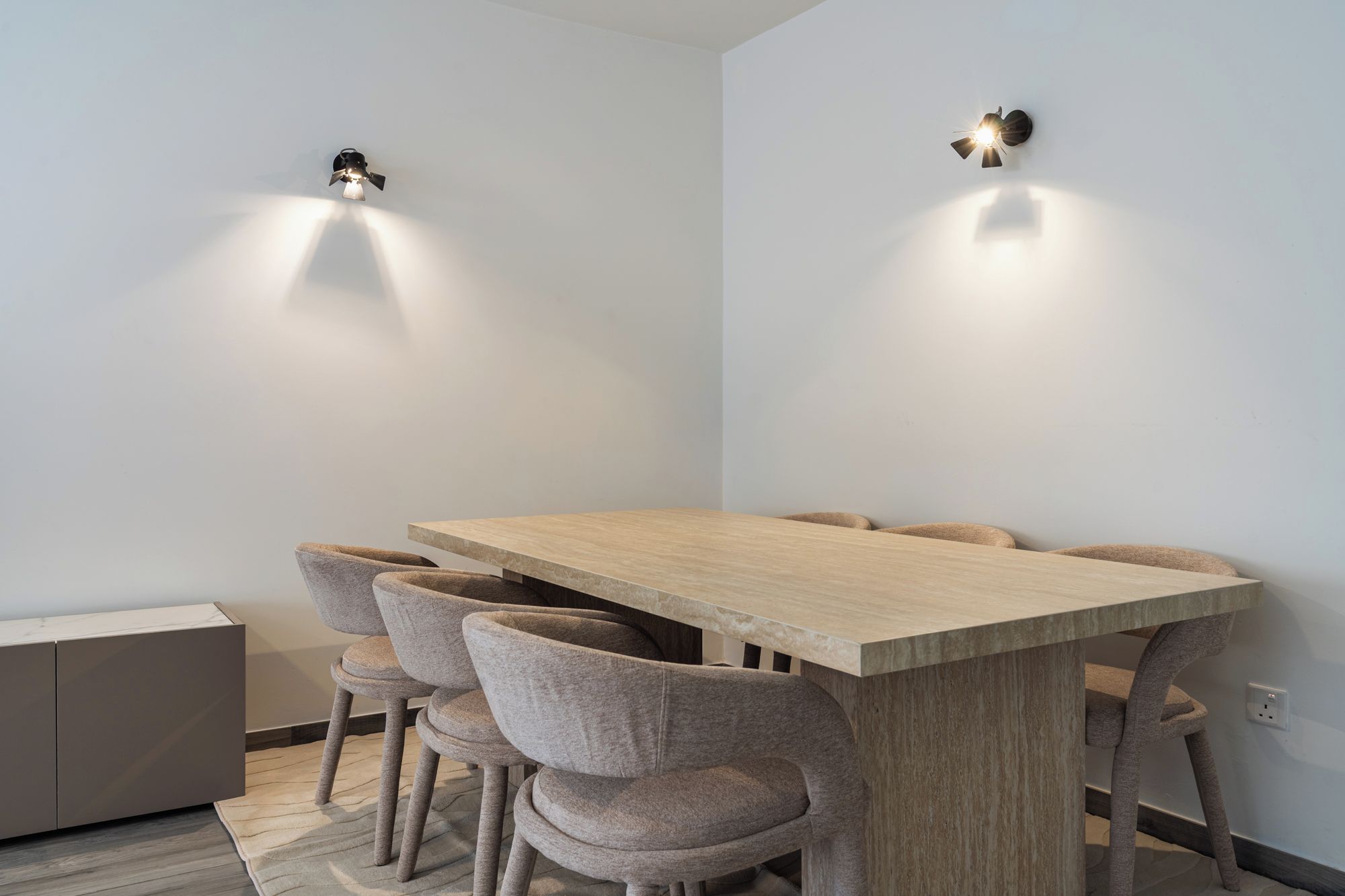 A modern dining area with a wooden table and matching chairs, two wall-mounted light fixtures, and a built-in cabinet.