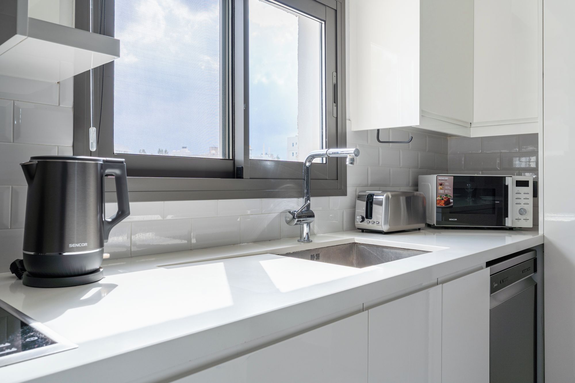 A modern kitchen with a stainless steel kettle, a toaster, and a microwave on the counter.