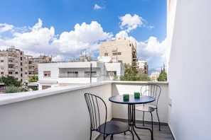 Un balcón con mesa y sillas, con vista a un paisaje urbano con varios edificios.