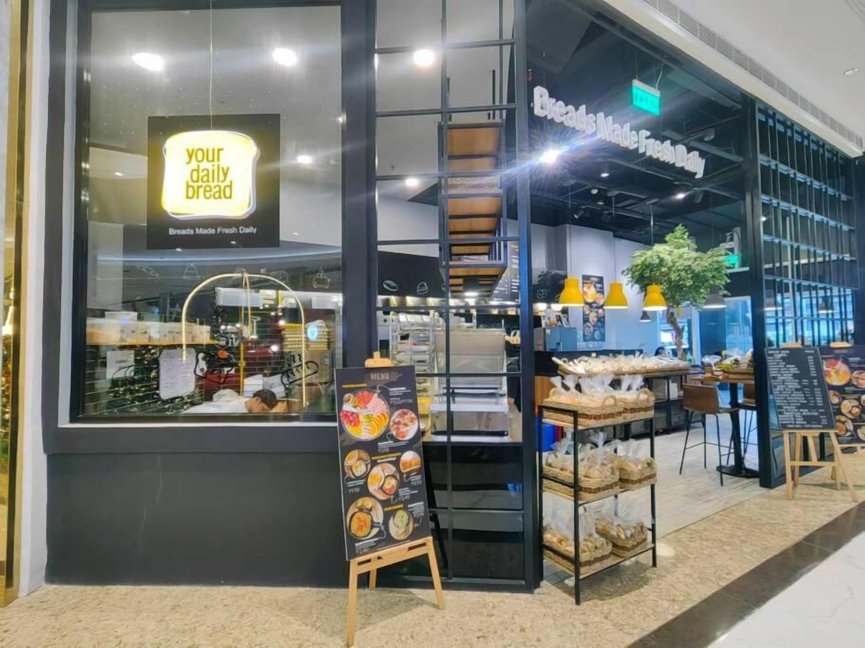 Eine Bäckerei mit einem Schild, das 'dein tägliches Brot' verkündet, und einer Speisekarte vor der Tür.