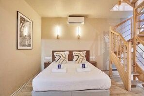 A bedroom with a bed, bedside tables, an air conditioning unit, a staircase, and a framed picture on the wall. - Modern duplex - Center of Paris Montorgueil (Paris)