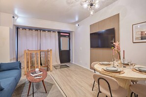 A modern living room with a sofa, a dining table set for four, a TV mounted on the wall, and a wooden rack. - Modern duplex - Center of Paris Montorgueil (Paris)