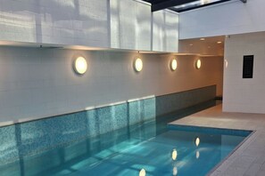 A swimming pool with a tiled edge, surrounded by white walls with recessed lighting. - Luxury City Retreat with Balcony Pool and Gym (Auckland)