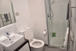 A modern bathroom with a white toilet, a sink, and a glass-enclosed shower area. - Luxury City Retreat with Balcony Pool and Gym (Auckland)